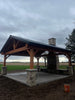 Wooden gazebo with a stone base in a field under a cloudy sky